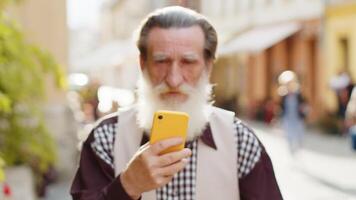 Senior man use smartphone typing text messages browsing internet finishing work looking at camera video