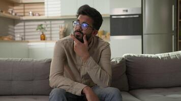 Pensive thoughtful Indian Arabian ethnic man puzzled guy at home apartment kitchen think difficult decision solve issue unhappy male rest alone on couch thinking deep thoughts consider doubt question video