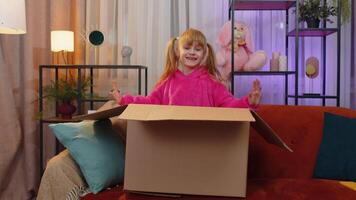 Happy toddler girl plays hide and seek jumping out of cardboard box, laughing, hiding inside package video