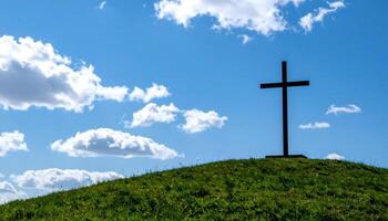 Silhouette of a cross standing on a grassy hill under a bright blue sky with white clouds. Perfect for ascension day jesus christ. photo