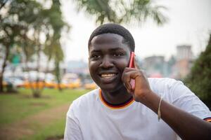 Portrait of an African boy making a phone call with his smartphone while outdoors in a public park. photo