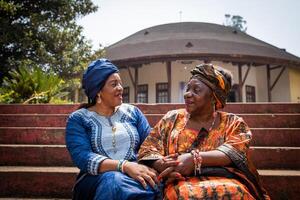Two African women are conversing sitting on the stairs, they are both dressed in traditional clothes photo