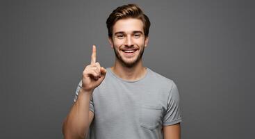 Portrait of smiling young man pointing finger on gray background photo