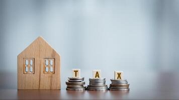 Wooden house model and coin stack with TAX word on wooden table. photo