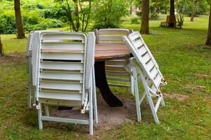 Empty outdoor dining area with stacked chairs against a wooden table surrounded by green scenery in a park photo