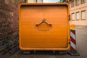 Bright orange dumpster standing out against the rustic architecture in a quiet European street during the day photo