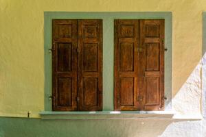 Intricate wooden shutters grace a charming yellow wall capturing the essence of rustic architecture in a serene setting photo