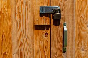 Bold wooden door with padlock and metallic handle illuminated by sunlight creates a rustic atmosphere in a countryside setting photo