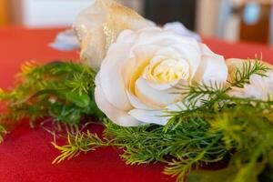 Beautiful white rose elegantly arranged on a vibrant red tablecloth with lush greenery, creating a stunning decor for a festive occasion photo