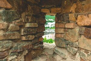 Exploring ancient stone walls and modern homes through a narrow window at sunset in a charming hillside town photo