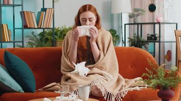 Sick ill woman suffering from cold or allergy sitting on home sofa sneezes wipes snot into napkin video