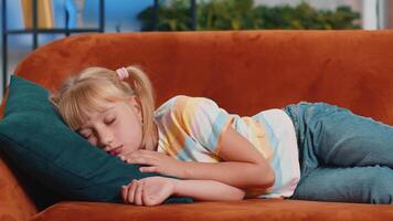 Tired school girl child kid lying down in bed taking a rest at home, napping, falling asleep on sofa video