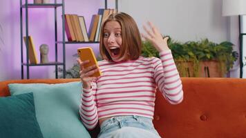Happy young woman at home use smartphone typing browsing wow yes found out great big win celebrate video
