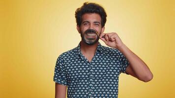 Indian man holding magnifier glass on teeth, looking at camera showing funny smiling face mouth video