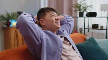 Tired asian man enjoy relaxing on home couch resting napping after hard working day, closed his eyes video