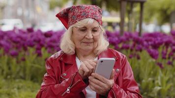 Senior woman use smartphone typing text messages browsing internet finishing work looking at camera video