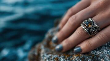 Hand resting on a rock with an ornate ring by the ocean during sunset hours photo