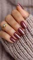Beautiful dark red manicure featuring glitter on long nails against a cozy knitted sweater backdrop photo