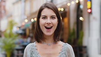 Young woman looking surprised at camera shocked by sudden win good victory news, wow in city street video
