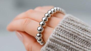 Hand wearing a shiny silver bracelet with textured round beads against a soft knit sweater background photo