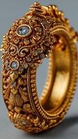 Intricately designed golden bangle with floral motifs and embedded stones displayed against a neutral background photo