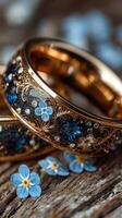 Elegant gold rings adorned with intricate designs and blue flowers on a rustic wooden surface photo