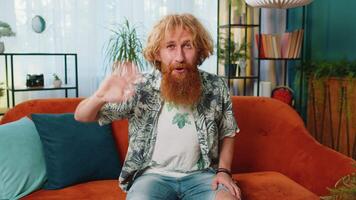 Caucasian man smiling friendly at camera, waving hands gesturing hello, hi, greeting at home on sofa video