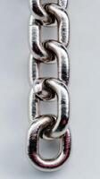Metallic chain hanging against a light background with reflections showcasing intricate details of each link photo