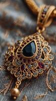 Elegant gold pendant featuring intricate design and dark gemstone against a textured fabric background photo