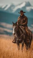 Cowboy riding horse in golden grasslands with mountains in the background during sunset photo