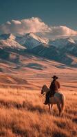 Cowboy on horseback surveying vast mountainous landscape at sunset in rural area photo