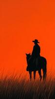 Silhouette of a cowboy on horseback against an orange sunset in a grassy field photo