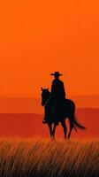 Cowboy silhouette against vibrant orange sunset over grassy plains photo
