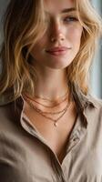 Elegant woman showcases layered gold necklaces indoors while wearing a stylish blouse and natural makeup photo