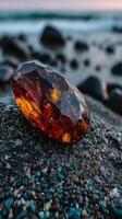 Unique amber stone rests on pebbled shore during sunset over the ocean waves photo