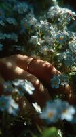 Close-up of a hand adorned with a ring, resting among delicate blue flowers in soft natural light photo