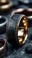 Black and gold wedding band displayed among various rings in an artistic arrangement photo