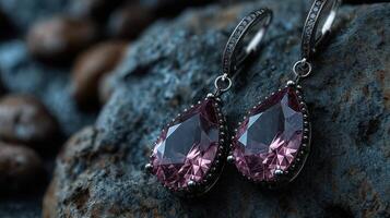 Elegant pink gem earrings resting on a textured stone surface with a dark background photo