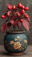 Decorative potted plant with vibrant red fruit and striking foliage placed against a neutral backdrop photo