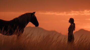 Silhouette of a woman and horse against a sunset in an open field with distant mountains photo