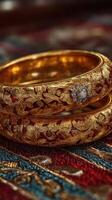 Intricate gold bangles with floral designs displayed on a vibrant fabric background photo