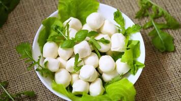 mini mozzarella in white bowl with greens on grey background. Top view video