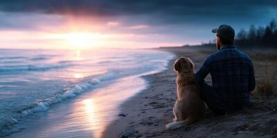 Man sitting on a beach with his dog watching a sunset over calm waters photo