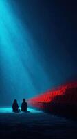 Two figures sit quietly in a dimly lit theater with red seats under a beam of blue light photo