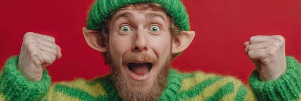 Enthusiastic man dressed as a festive elf celebrates joyfully against a vibrant red backdrop during a holiday event photo