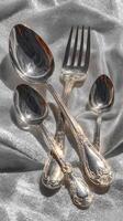 Beautifully arranged silver cutlery set reflecting light on a satin background in a timeless display photo