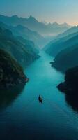 Misty mountains and calm river with a solitary boat navigating at dawn photo