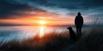 Person and dog enjoy a serene sunset walk by the water's edge photo
