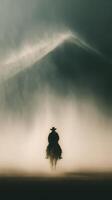 Cowboy rides through foggy landscape with mountains in background during early morning hours photo