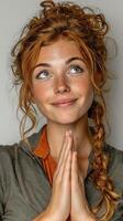 Young woman with curly red hair smiles with hands clasped together, expressing joy indoors photo